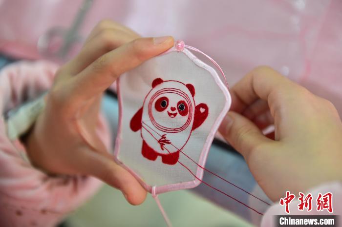 圖為一名小學生正在繡制2022年北京冬奧會吉祥物“冰墩墩”形象?！∮髟屏?攝