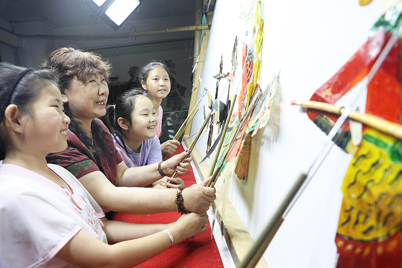 皮影藝人指導小朋友表演皮影戲。