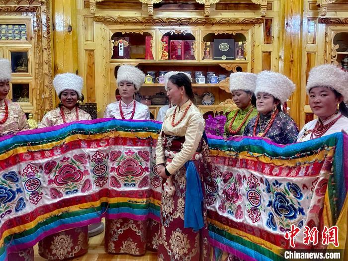 圖為女性展示村民自發(fā)繡制的“百米五彩哈達(dá)”?！±钣穹?攝